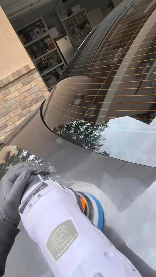 Polishing out a scratch on the rear glass surround of a dark sedan