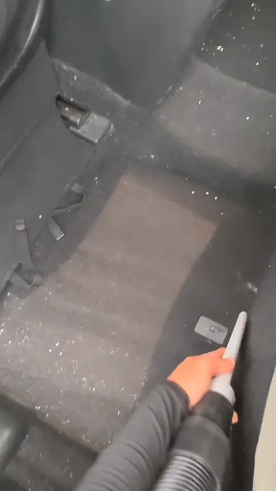 Vacuuming the rear carpet of a sedan