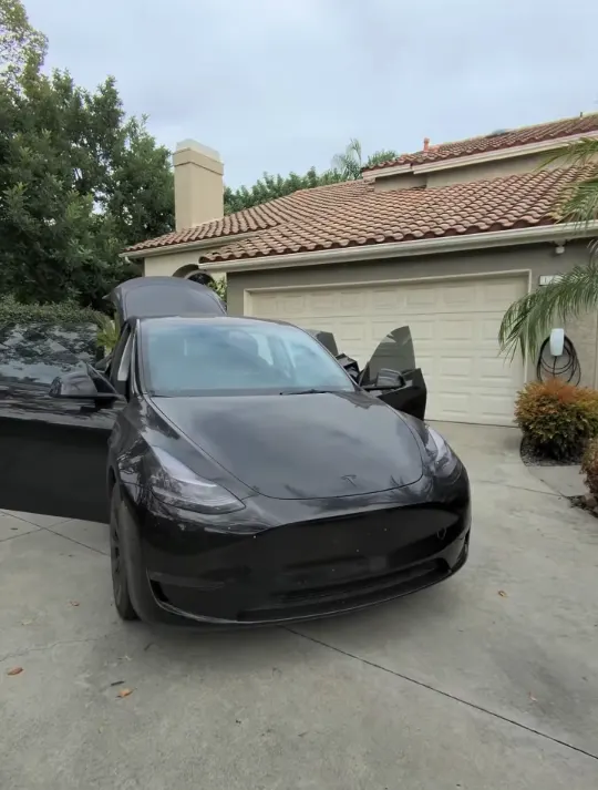 Black Tesla Model Y in a driveway before its detail, doors open